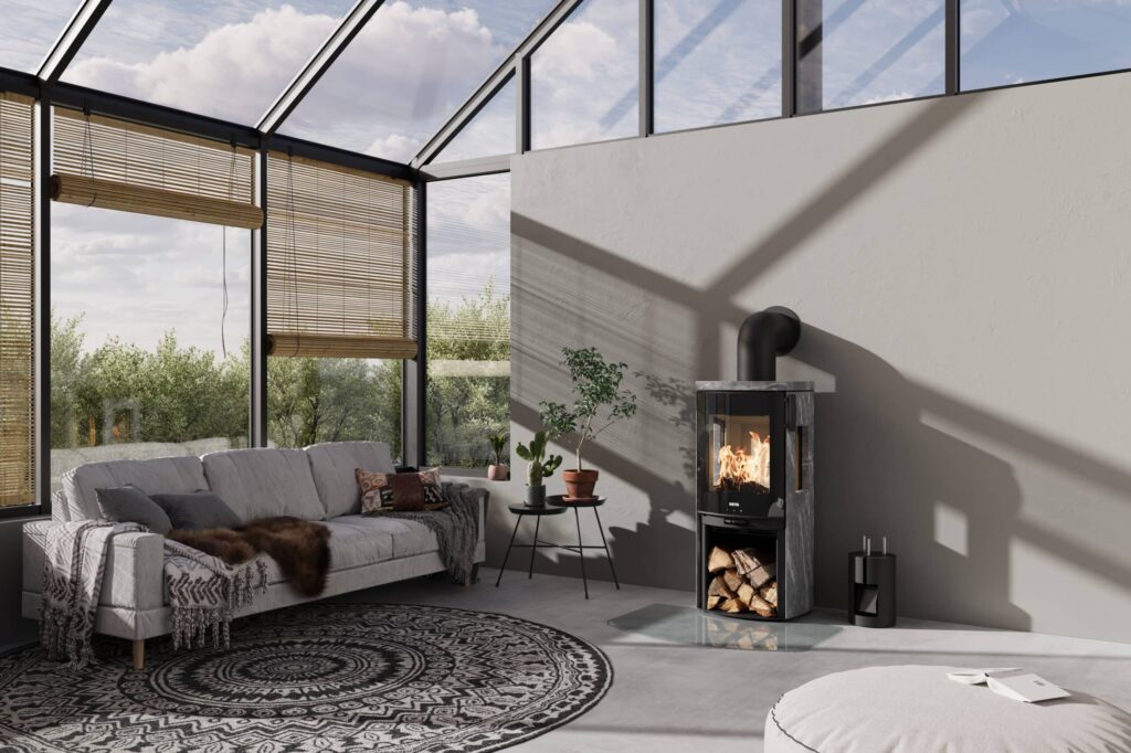 Tänd braskamin med svart front och sidor i grå täljsten placerad mot en ljusgrå vägg